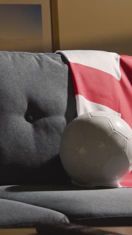 Vertikales-Video-Eines-Sofas-In-Der-Lounge-Mit-Englischer-Flagge-Und-Ball,-Während-Sich-Die-Fans-Darauf-Vorbereiten,-Fußballspiele-Im-Fernsehen-Zu-Sehen